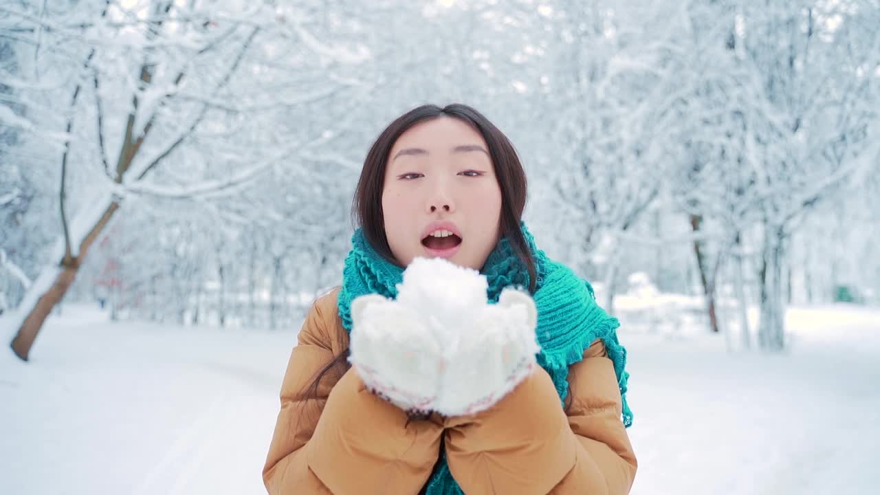 美丽冬天亚洲女孩吹雪在霜冻的冬天公园。在户外。飞的雪花。年轻女子在寒冷的户外玩耍。快乐视频素材