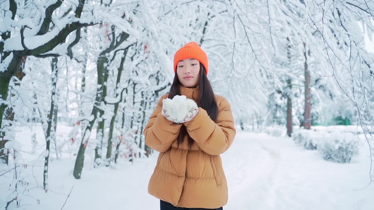 美丽冬天亚洲女孩吹雪在霜冻的冬天公园。在户外。飞的雪花。年轻女子在寒冷的户外玩耍。快乐视频素材