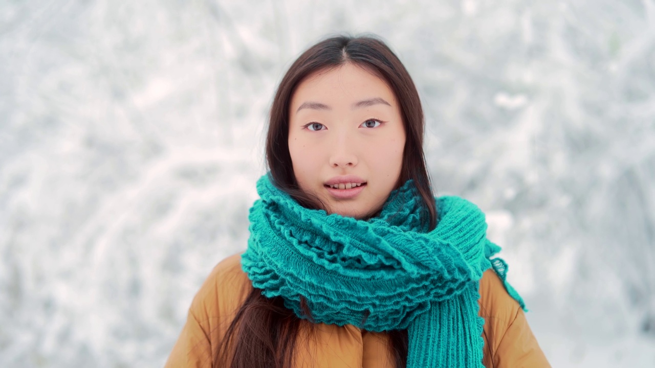 美丽的肖像年轻的亚洲妇女站在雪地背景在公园在寒冷的天气，看着相机。年轻快乐微笑的美丽女孩的脸在冬天的户外视频素材