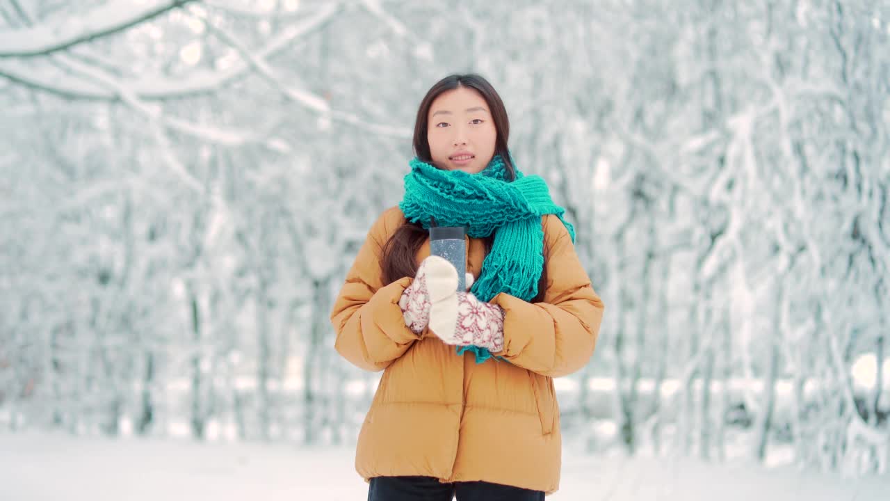 快乐开朗的亚洲女孩走在下雪的公园或森林在冬天。在寒冷的天气里，年轻迷人的女子走在白雪背景的户外视频素材