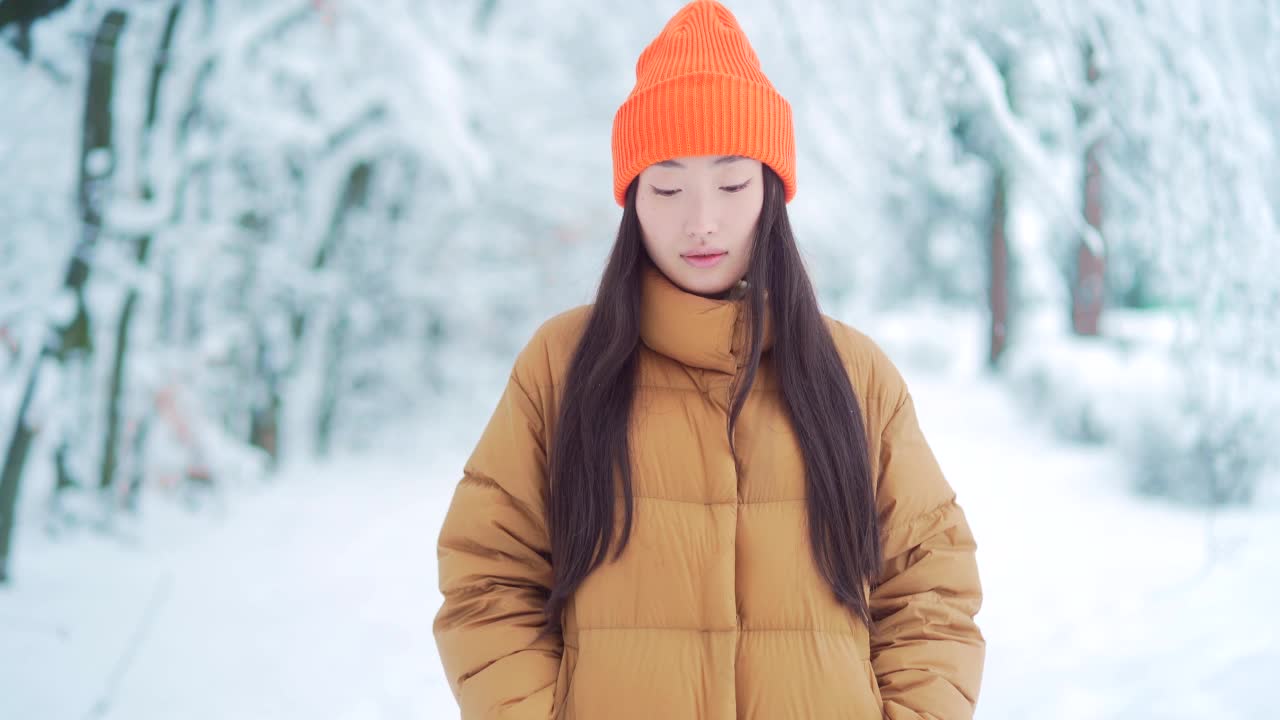 美丽的肖像年轻的亚洲妇女站在雪地背景在公园在寒冷的天气，看着相机。年轻快乐微笑的美丽女孩的脸在冬天的户外视频素材