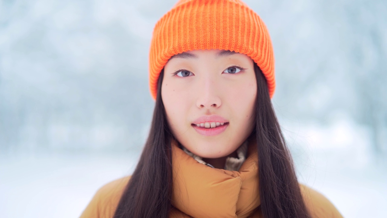 美丽的肖像年轻的亚洲妇女站在雪地背景在公园在寒冷的天气，看着相机。年轻快乐微笑的美丽女孩的脸在冬天的户外视频素材