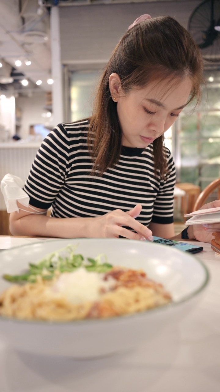 亚洲妇女在餐厅边吃意大利菜边看手机视频素材