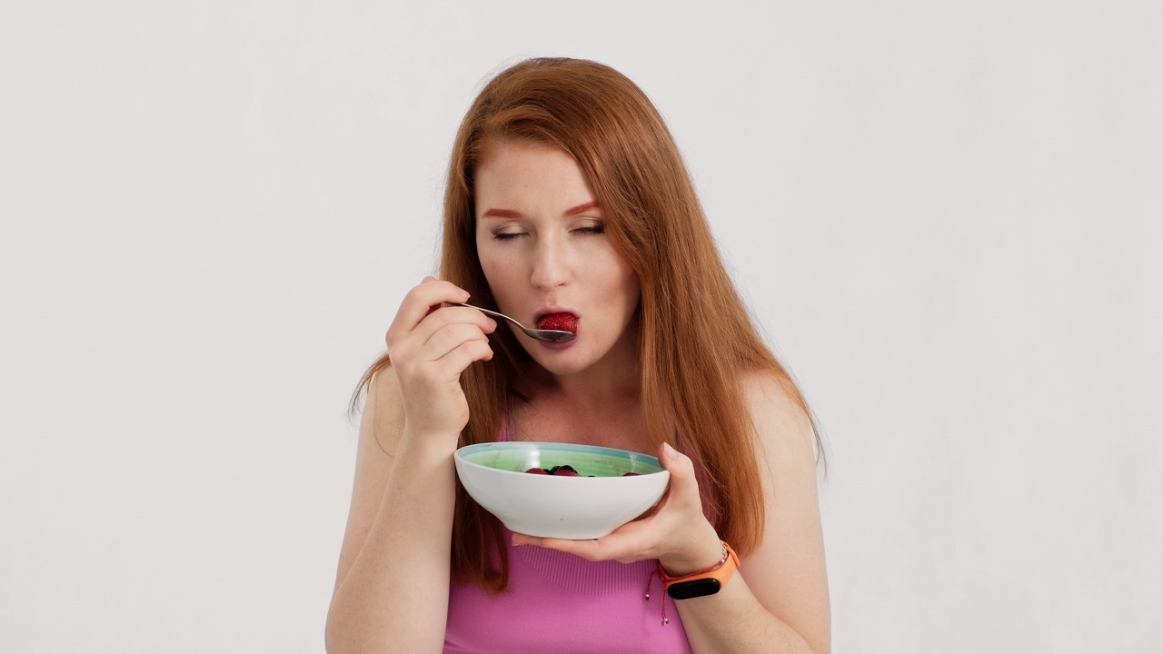 年轻女子在白底上吃草莓。季节性的食物。视频素材