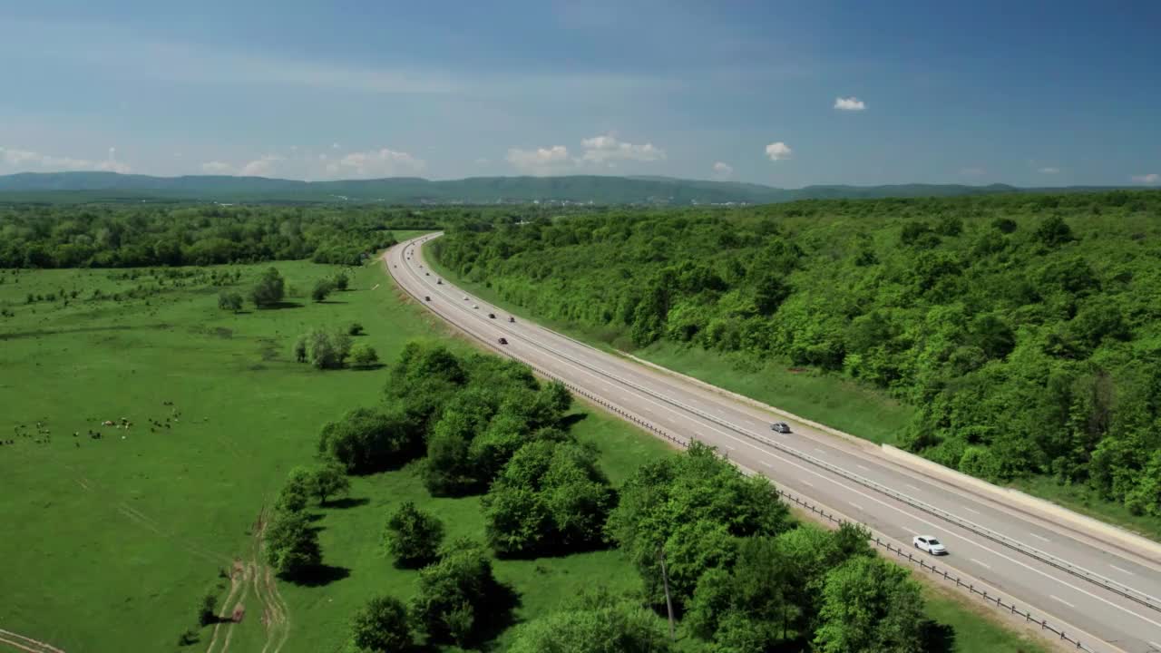 在高速城际公路上的空中飞行，车辆在公路上行驶。夏天阳光明媚的一天，附近有森林和农村的田野视频素材