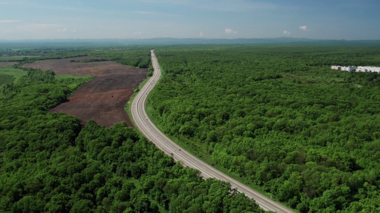 在高速城际公路上的空中飞行，车辆在公路上行驶。夏天阳光明媚的一天，附近有森林和农村的田野视频素材