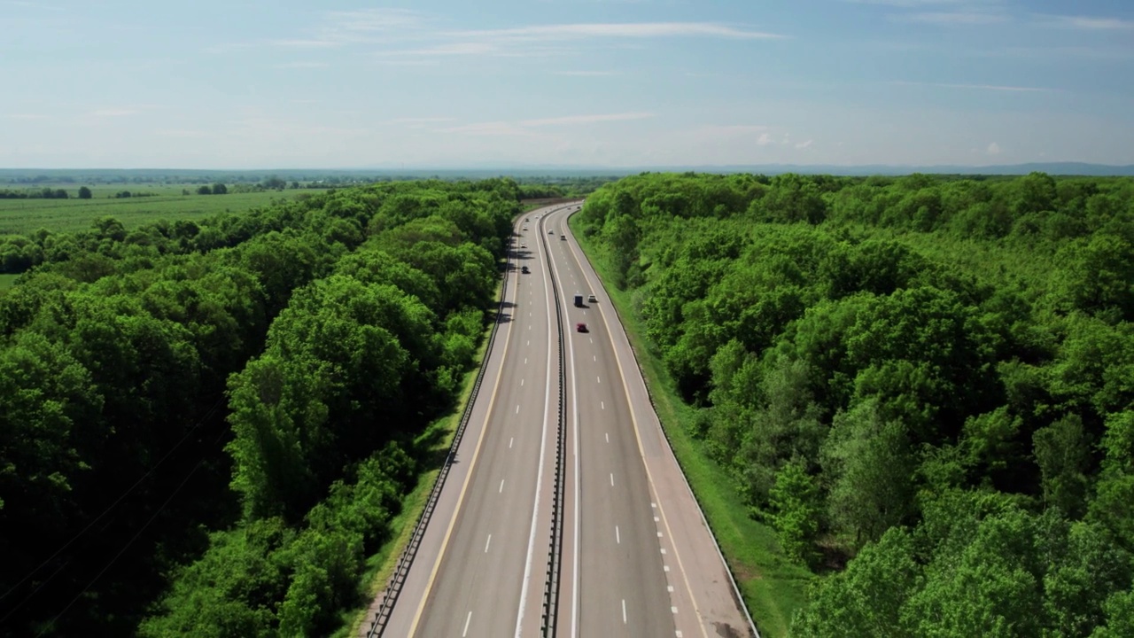 在高速城际公路上的空中飞行，车辆在公路上行驶。夏天阳光明媚的一天，附近有森林和农村的田野视频下载