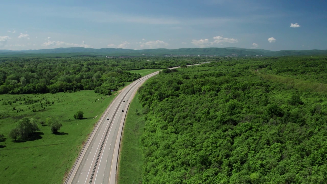 在高速城际公路上的空中飞行，车辆在公路上行驶。夏天阳光明媚的一天，附近有森林和农村的田野视频素材