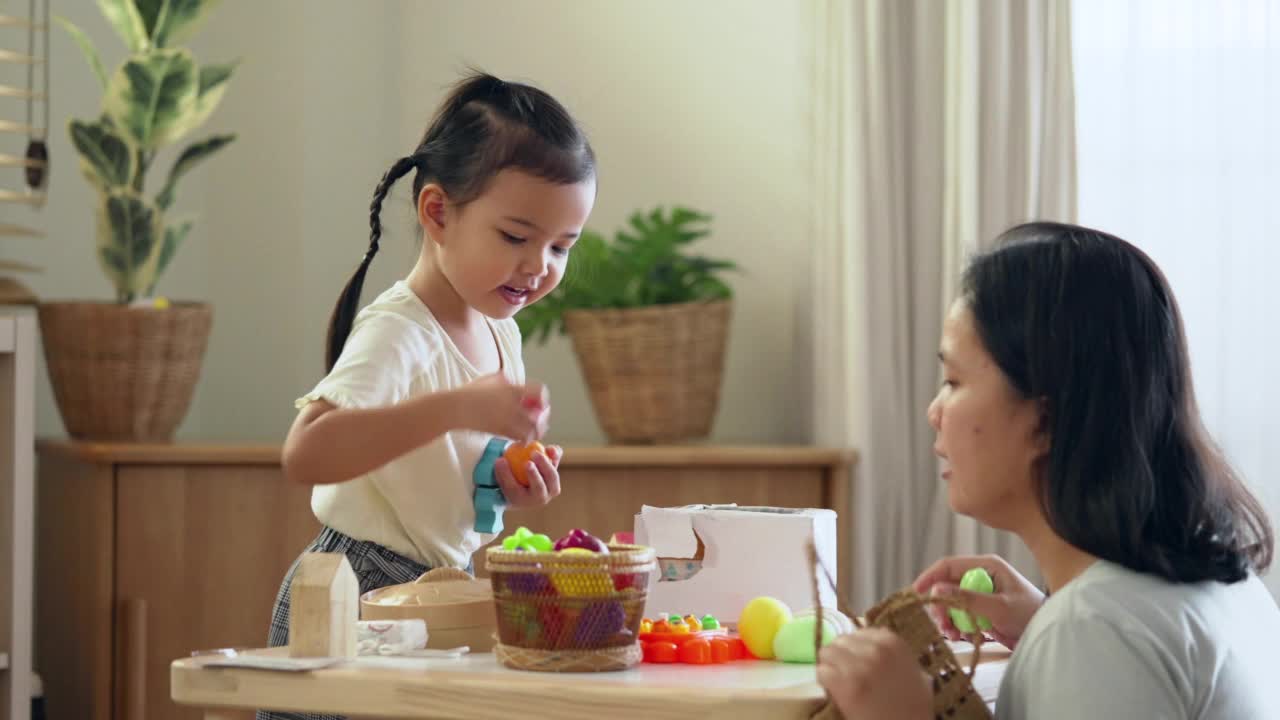 亚洲母亲和女儿喜欢周末在家里的客厅里一起玩儿童玩具。幸福的家庭时刻与孩子的教育视频素材