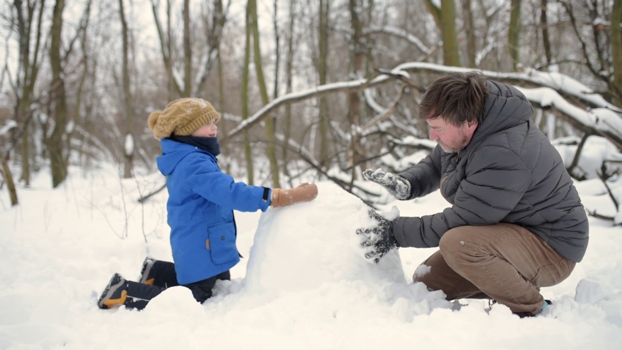 小男孩和他的父亲在雪地公园堆雪人。爸爸和儿子在一起度过了美好的时光。冬天与家人和孩子一起进行户外休闲活动视频素材