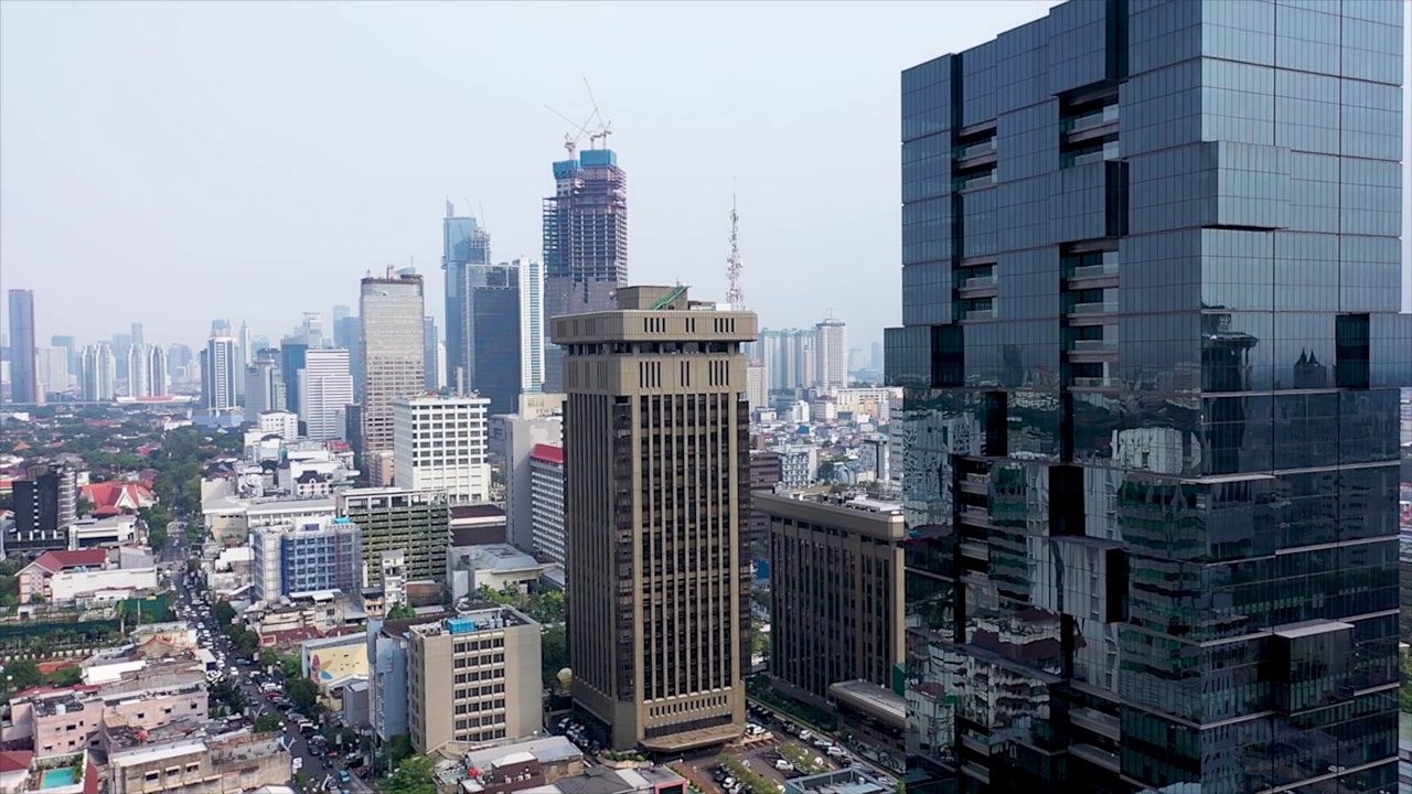 无人机在雅加达市商业中心的现代未来主义摩天大楼之间垂直飞行，夕阳反射在闪亮的玻璃立面上视频素材