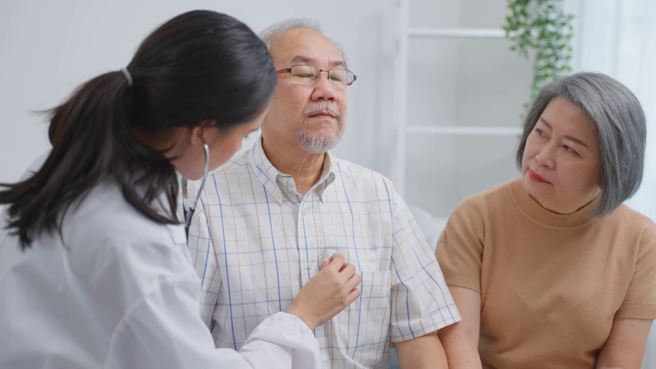 亚洲护工护士在家中检查老年男性患者及其妻子。有吸引力的年轻专业护工，妇女支持，给建议和咨询与年长，年长，成熟的夫妇在客厅里在房子里视频素材