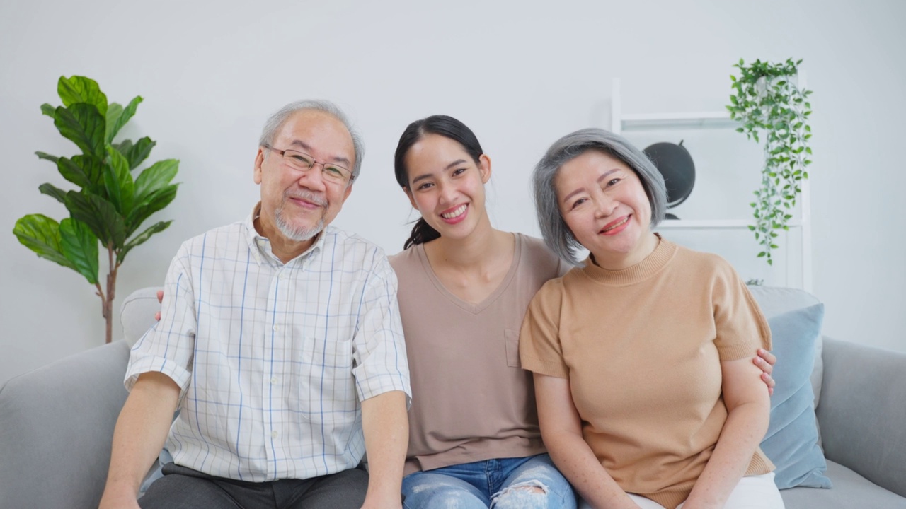 画像的亚洲高级老夫妇坐在年轻的女儿在房子。迷人美丽的孙女拜访年迈成熟的爷爷奶奶然后微笑着，在家里的客厅一起看镜头视频素材