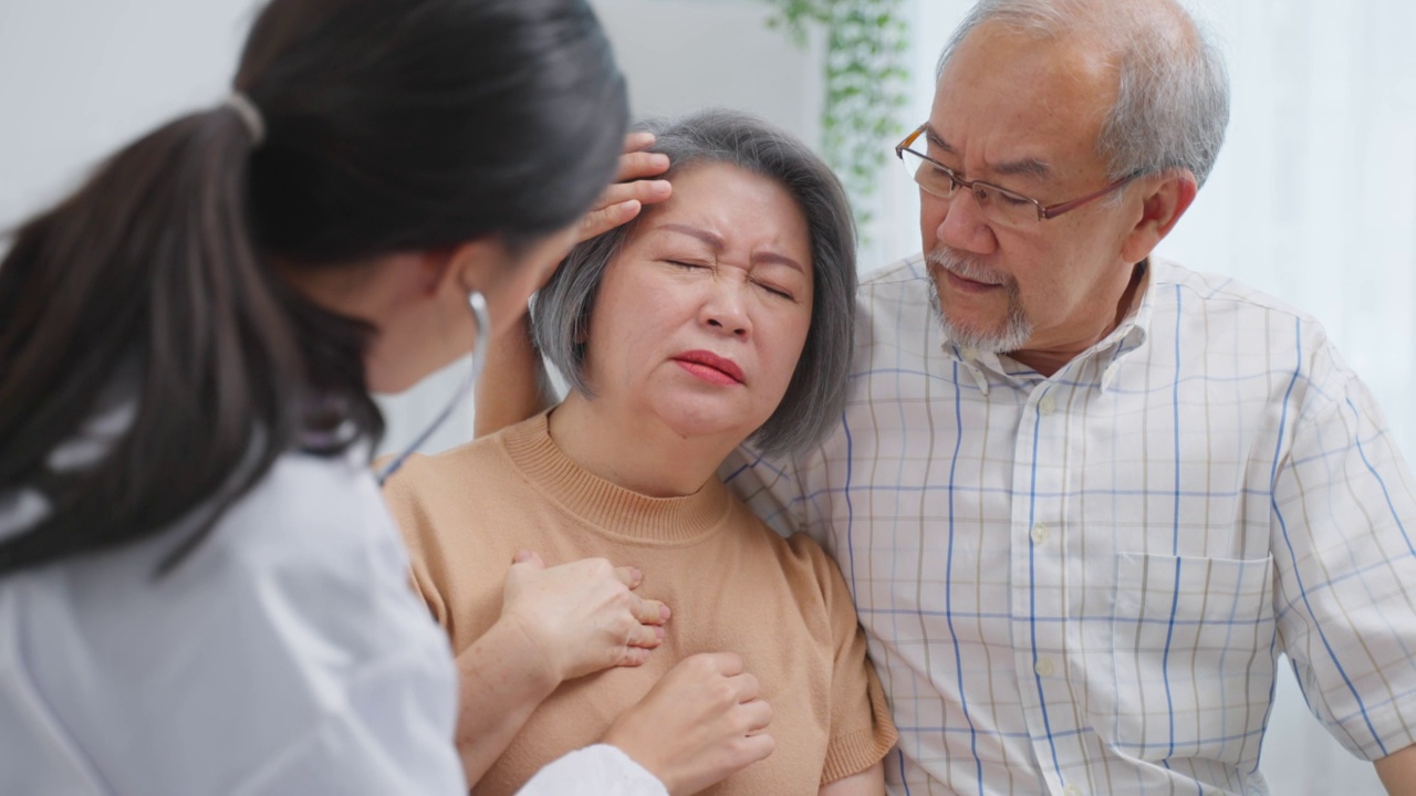 亚洲护工护士在家中检查老年男性患者及其妻子。有吸引力的年轻专业护工，妇女支持，给建议和咨询与年长，年长，成熟的夫妇在客厅里在房子里视频素材