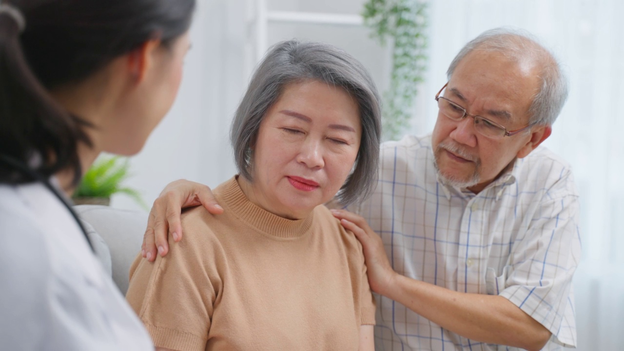 亚洲护工护士在家中检查老年男性患者及其妻子。有吸引力的年轻专业护工，妇女支持，给建议和咨询与年长，年长，成熟的夫妇在客厅里在房子里视频素材