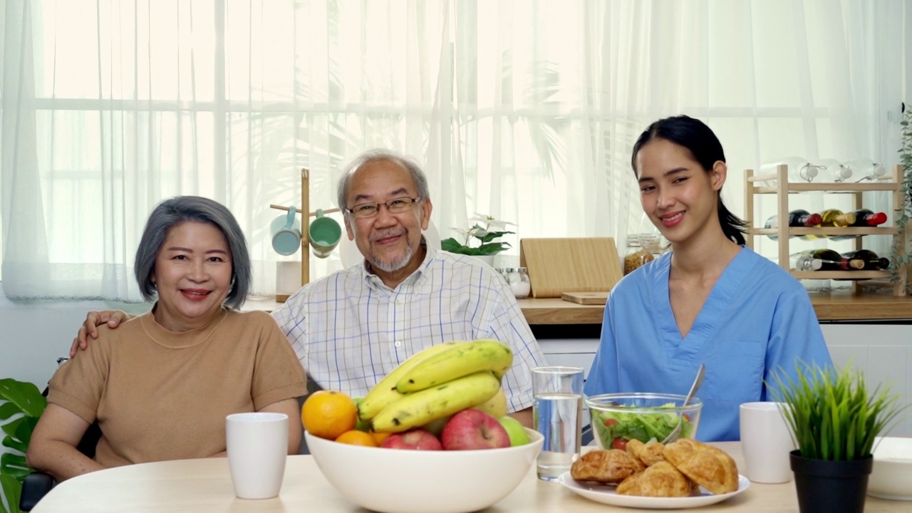 放大的亚裔老年祖父母和家庭护理护士正坐在餐桌上，有很多食物。视频素材