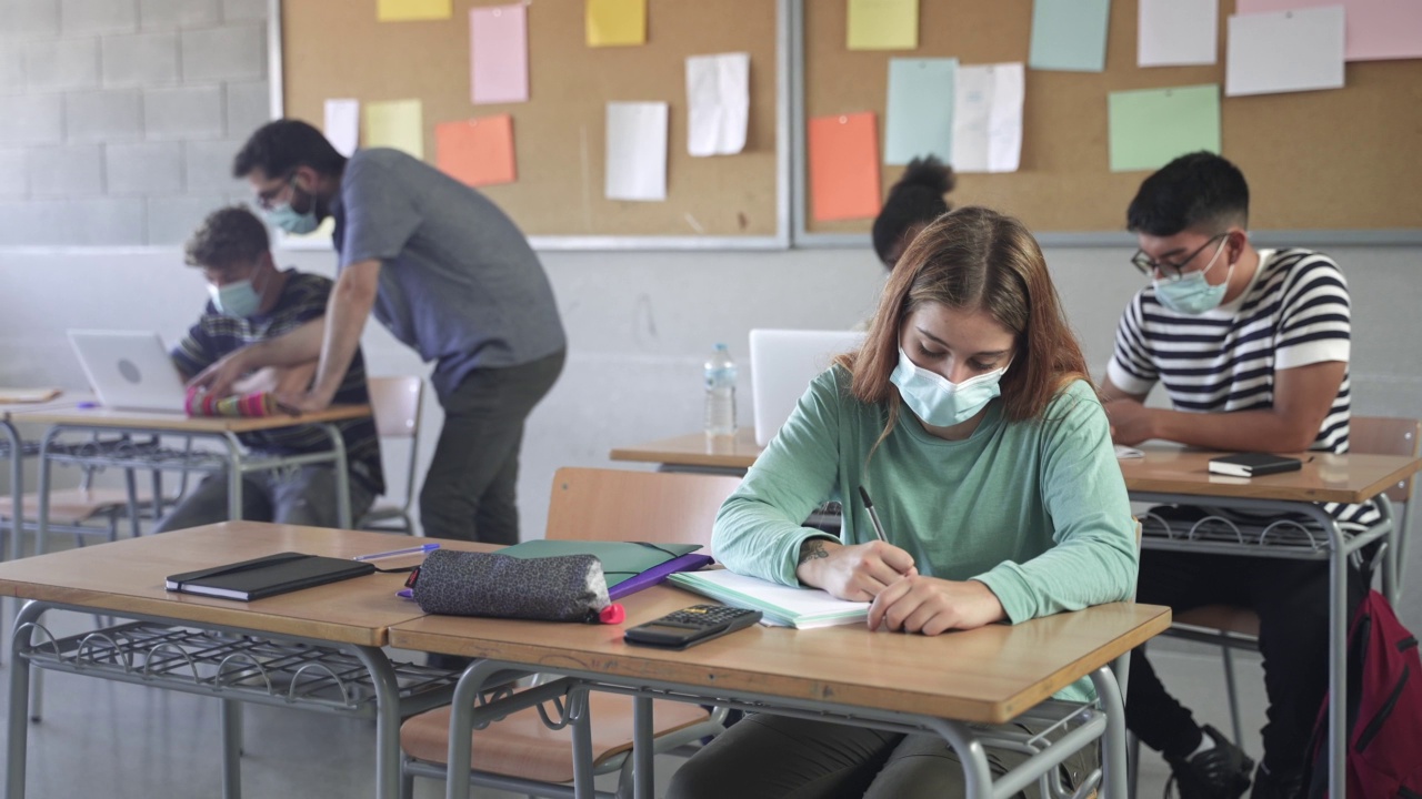 青少年戴着口罩学习，在学校写作业。在大学帮助学生的老师视频素材