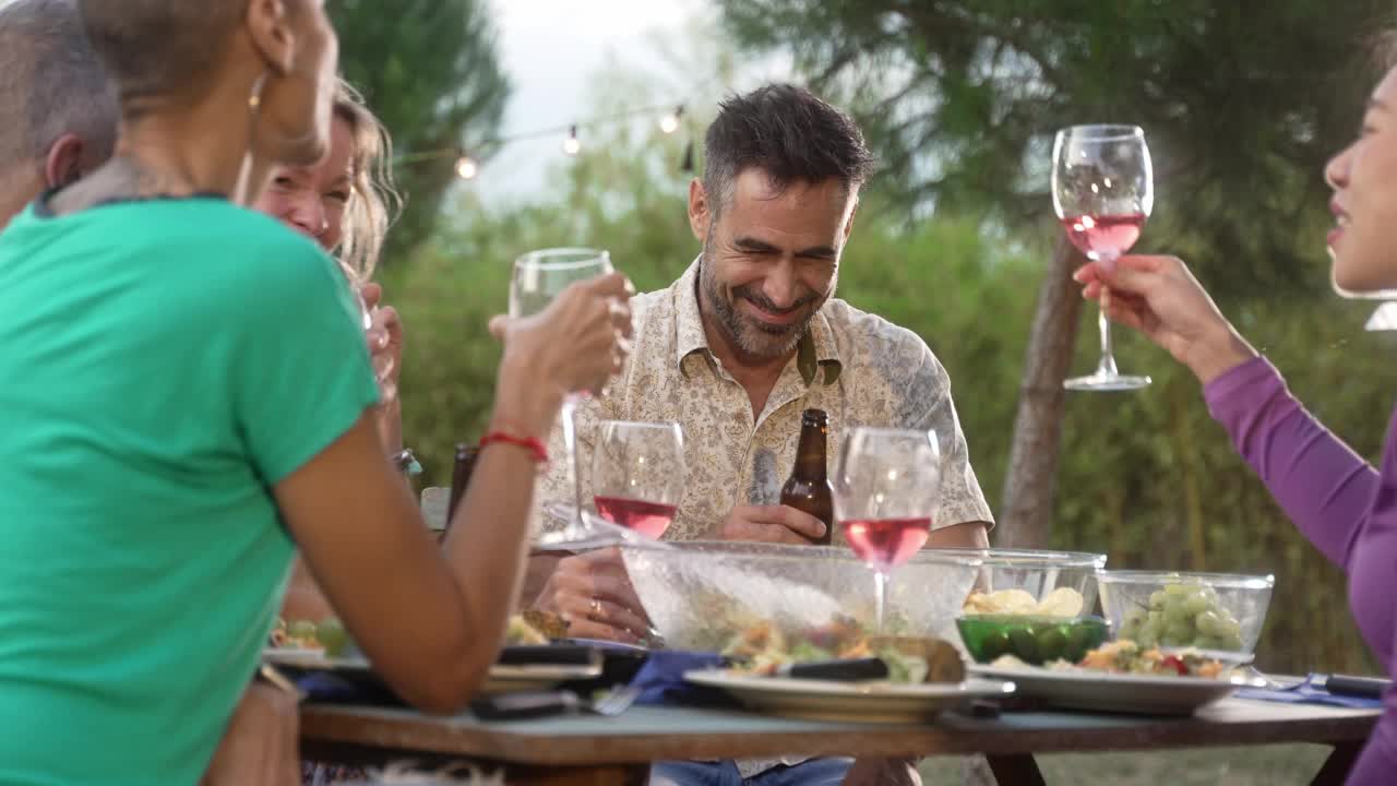 英俊的西班牙男子与朋友在花园里的夏日晚餐中举杯祝酒视频素材