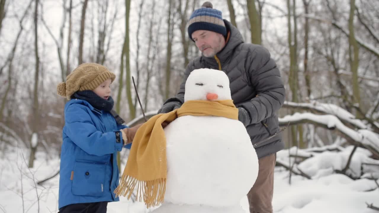 小男孩和他的父亲在雪地公园堆雪人。爸爸和儿子在一起度过了美好的时光。冬天与家人和孩子一起进行户外休闲活动视频素材