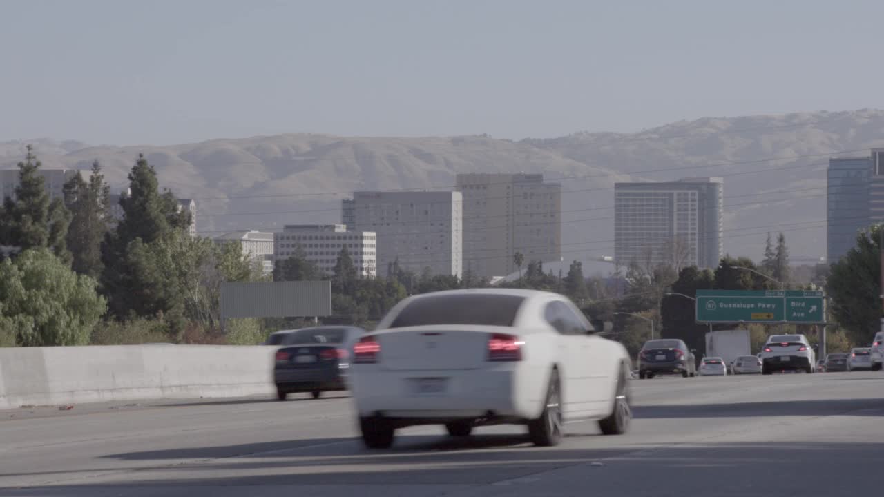 中等角度的汽车，卡车，公共汽车和越野车行驶在高速公路上。汽车从左向右移动。在bg可以看到圣何塞市的天际线视频素材