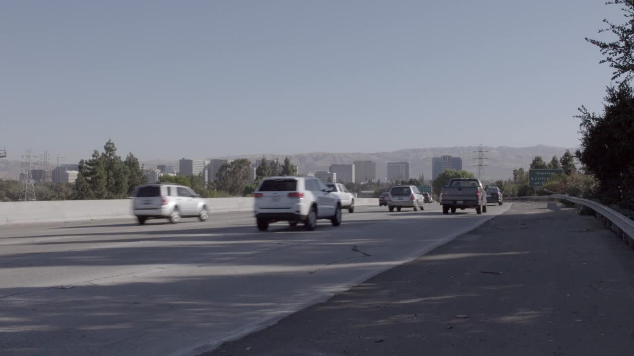 广角的汽车，卡车，公共汽车和越野车行驶在高速公路上。汽车从左向右移动。镜头放大到bg的圣何塞市的天际线视频素材