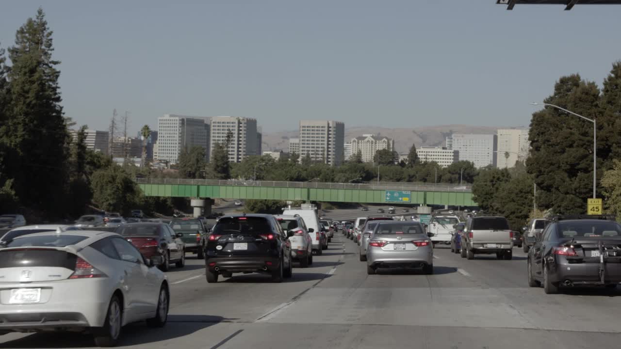 在高速公路或交通繁忙的高速公路上行驶的汽车的中角度驾驶pov。立交桥上的标志写着“87号公路”。在bg可以看到城市天际线视频素材