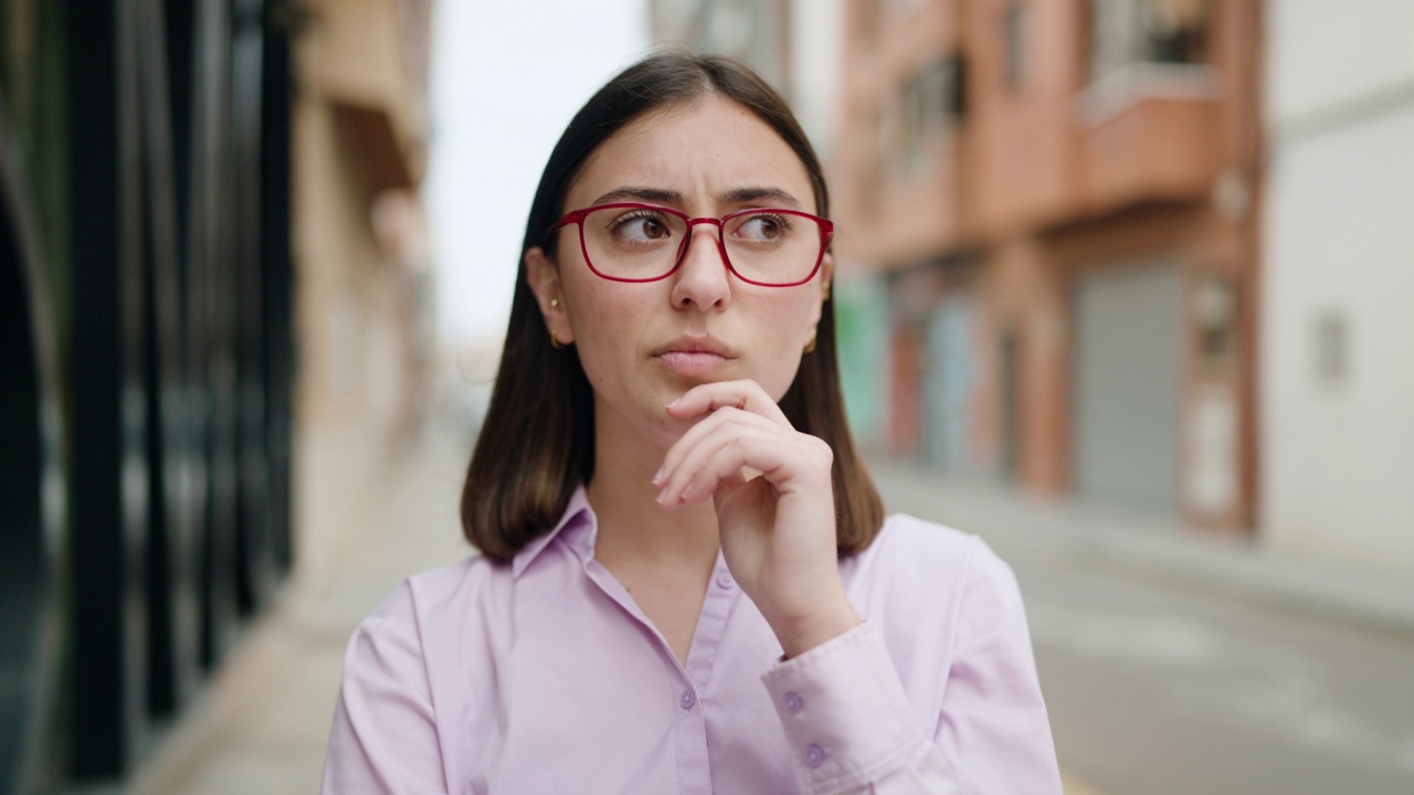 年轻的西班牙妇女戴着眼镜站在街上，带着怀疑的表情视频素材