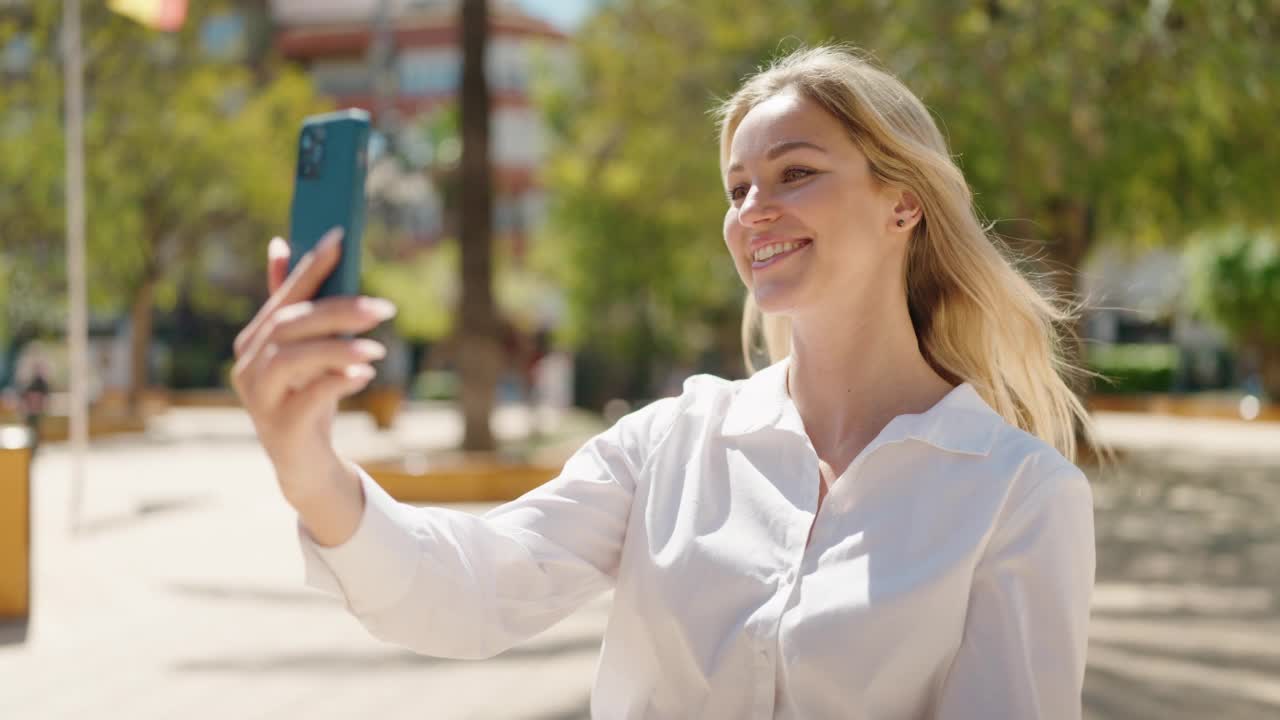 年轻的金发女子微笑自信的视频电话在公园视频素材