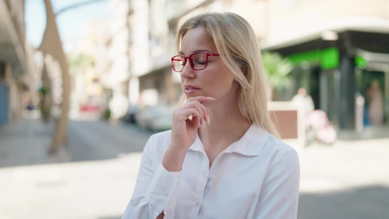 年轻的金发女人站在街上，带着怀疑的表情视频素材