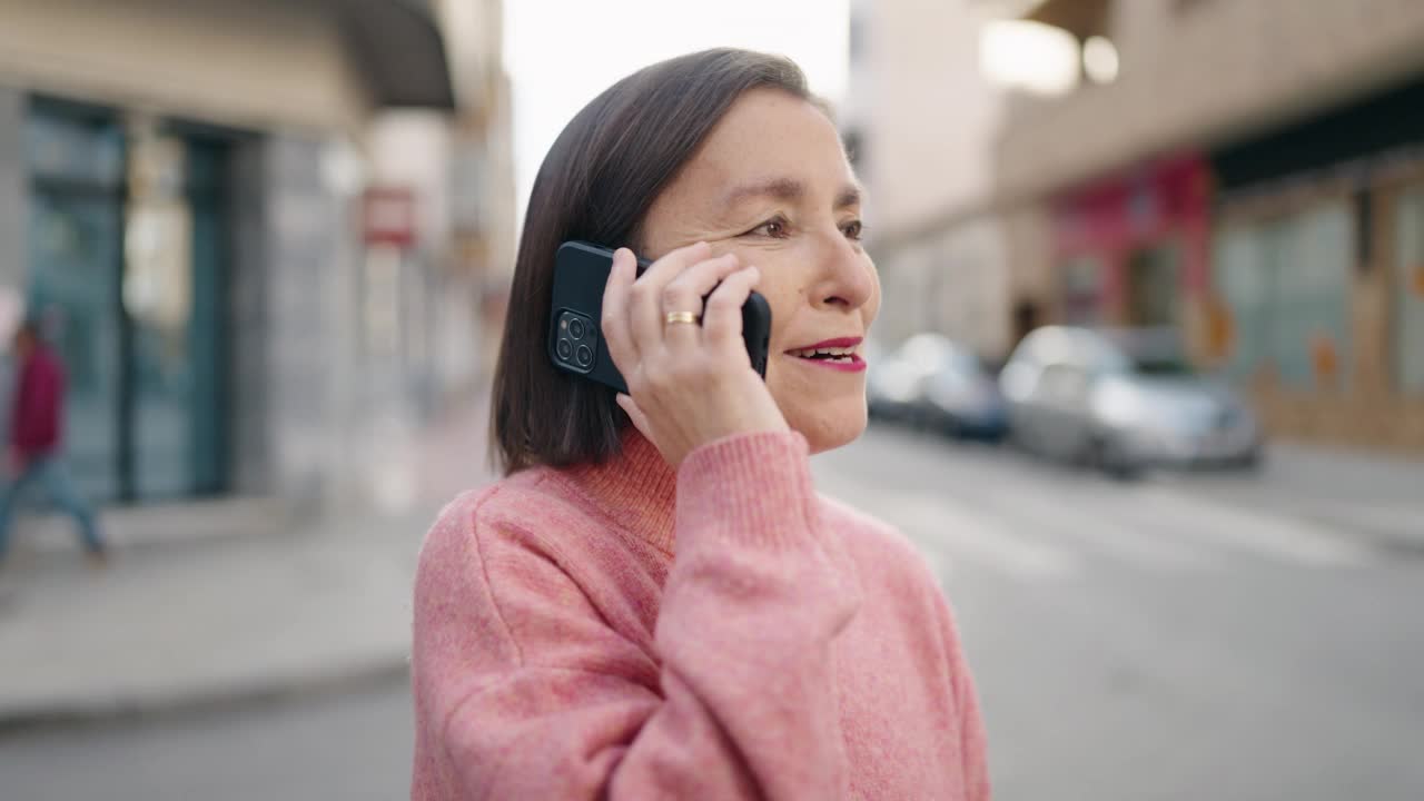 中年妇女微笑着自信地在街上用智能手机说话视频素材