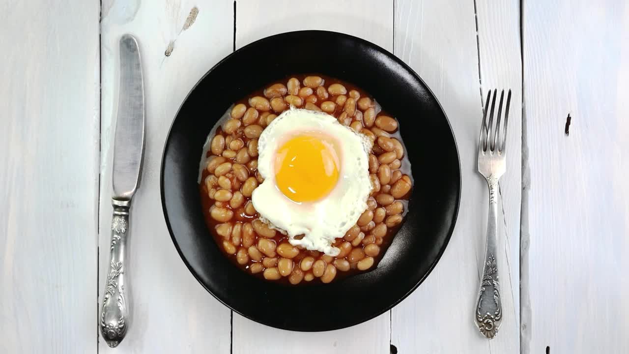 把黄烘豆煎蛋翻转在厨房木桌上的黑色盘子里。视频素材