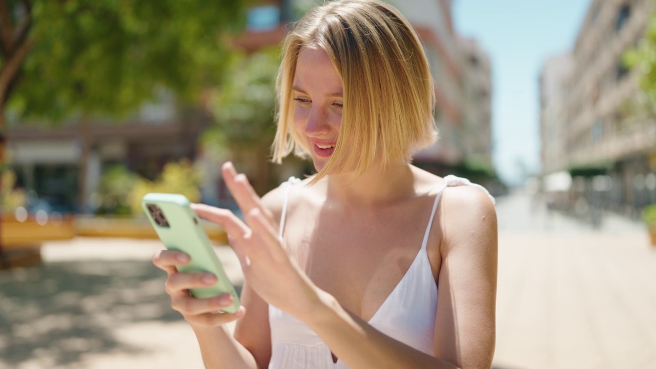 年轻的金发女子在公园里用智能手机散步视频素材