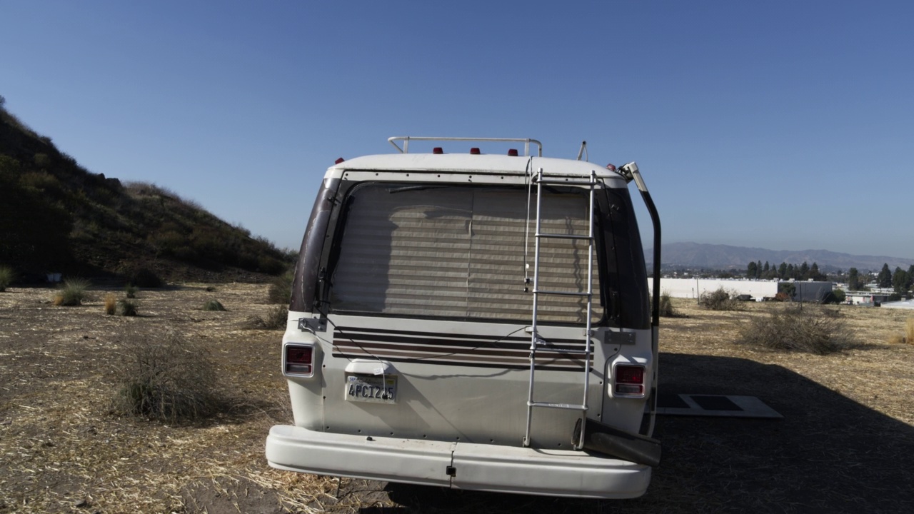 把停在工业区附近干燥山坡上的露营车或房车的窗户从近角度拉回。摄像机在露营车周围平移，拉回高角度向下。Suv和汽车停在rv附近视频素材