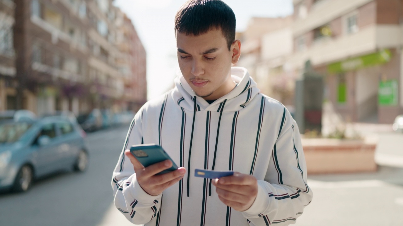 年轻男子在街上使用智能手机和信用卡视频素材