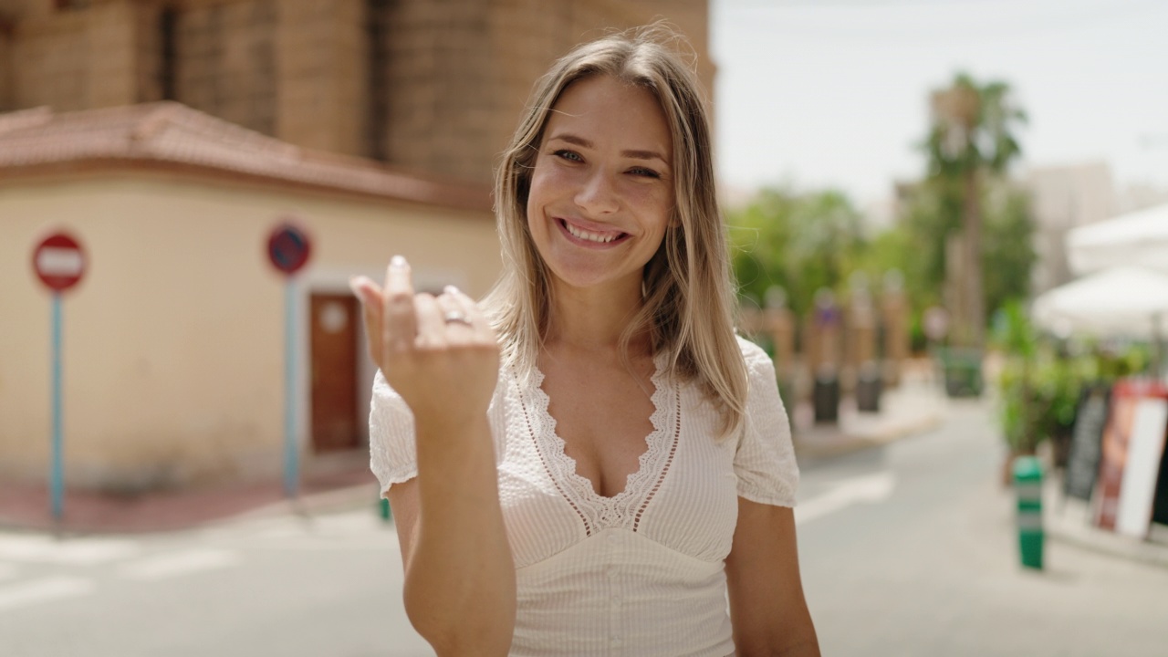 年轻的白人妇女微笑着自信地用手指指着街道做走过来的手势视频素材