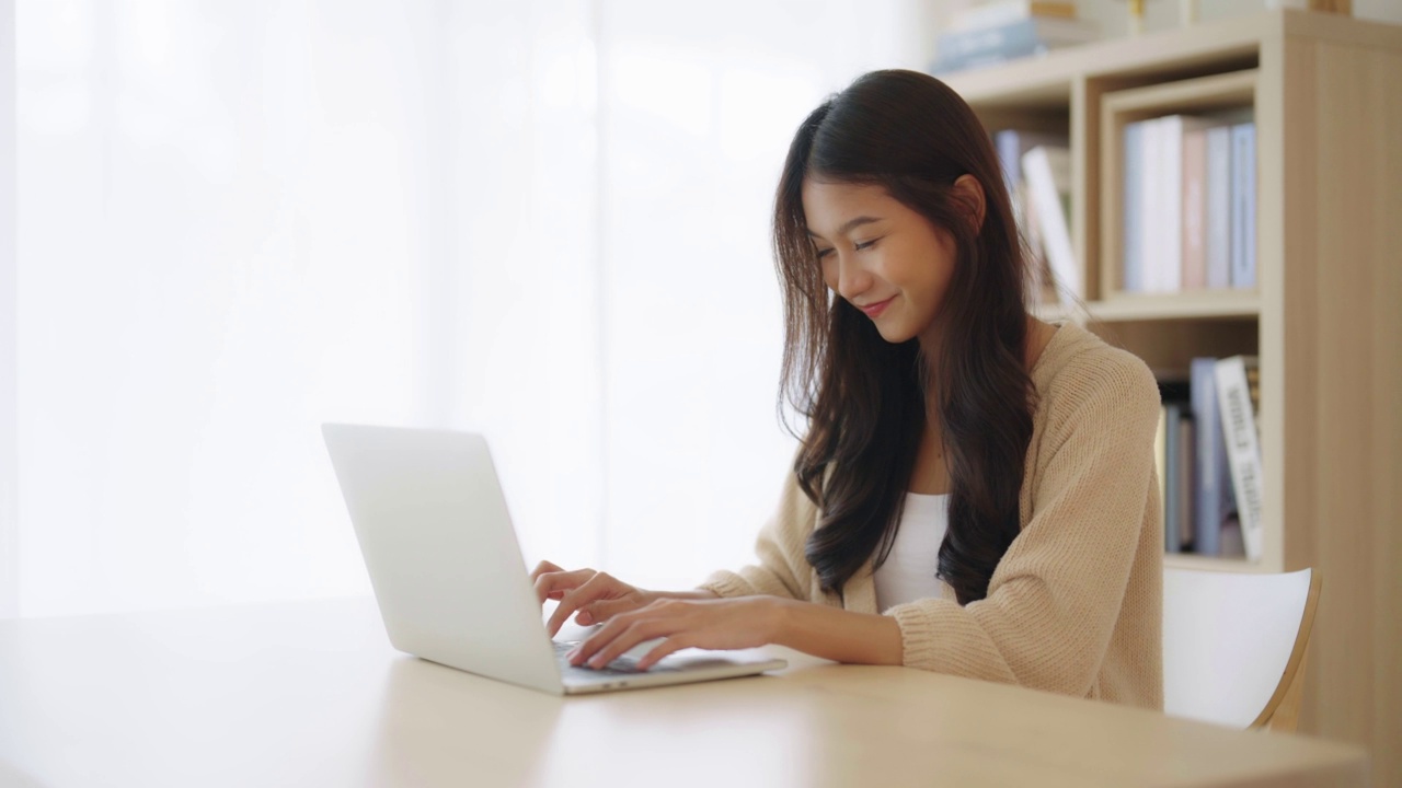 年轻的亚洲女性在家工作。女性在家里的桌子上使用笔记本电脑视频素材