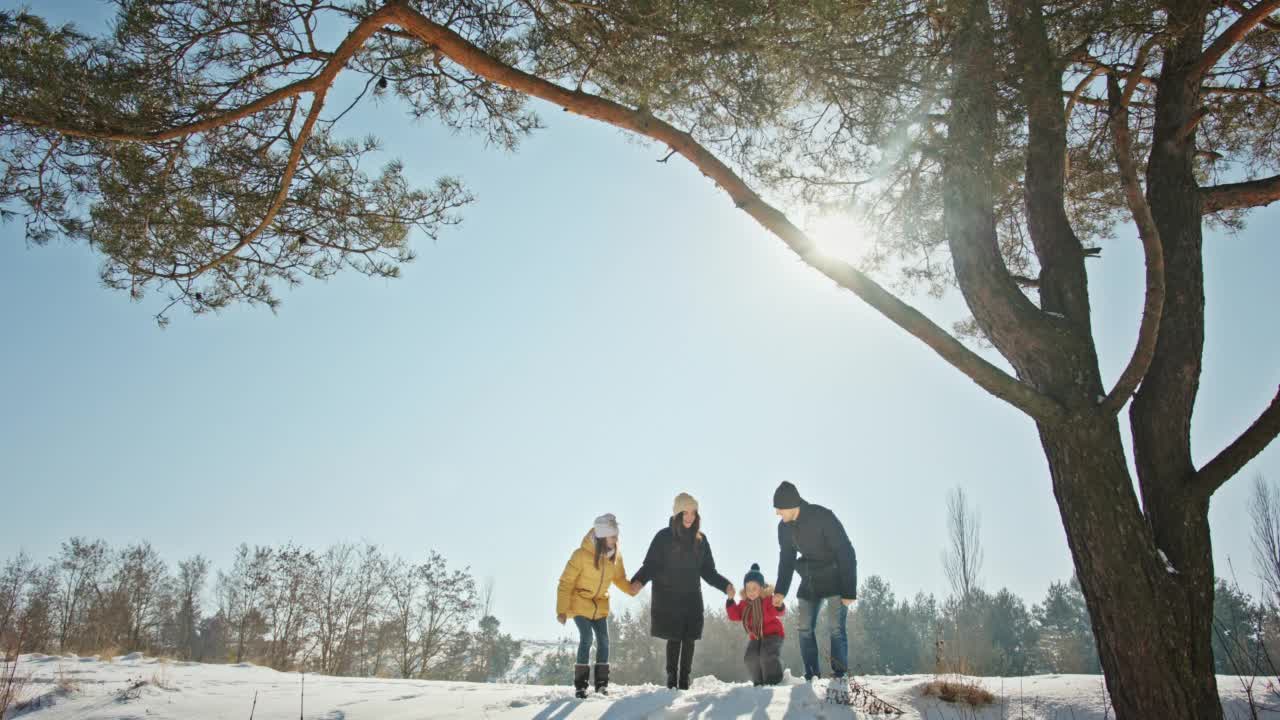 一家人在高松树旁的雪山上蹦蹦跳跳视频素材