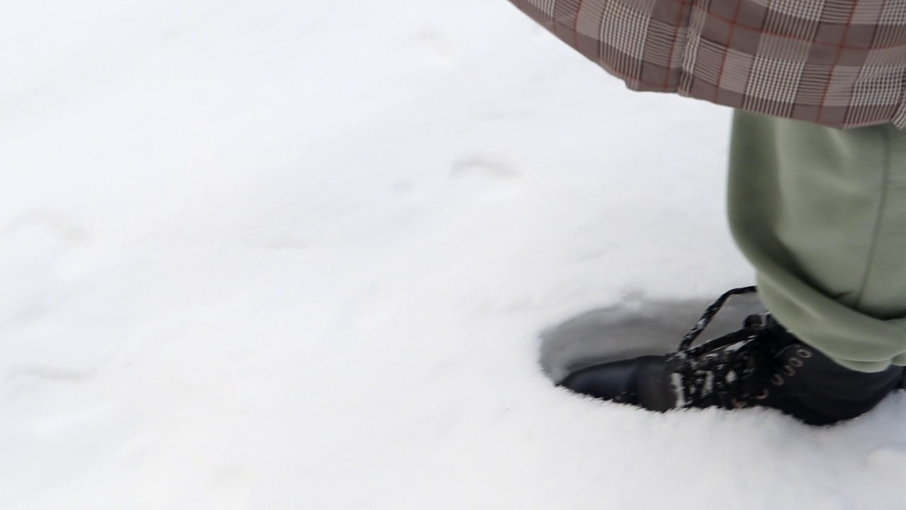 一个女人走在冬天森林的雪地上，靴子在新雪上留下脚印。一个穿着黑靴子的女人的腿，神秘而神秘地走在冬天的雪地里。低角度。视频素材