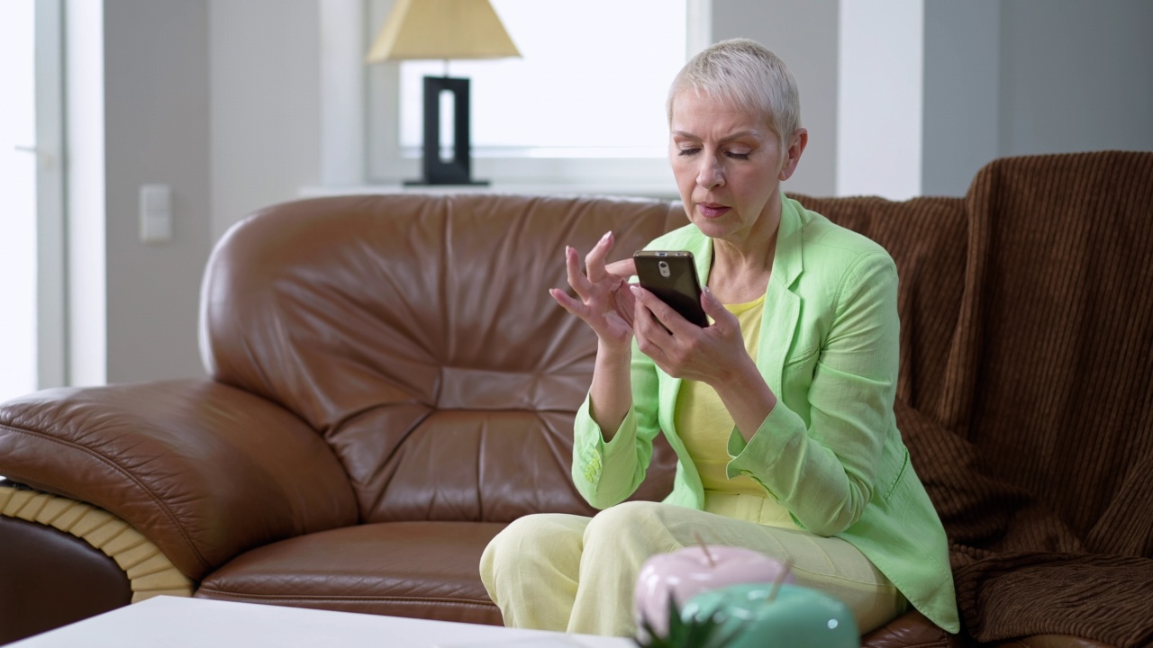 专注的女人用手机应用程序把购物袋放在桌子上。自信的白人中年购物者在网上购物微笑的肖像。便利和现代科技。视频素材