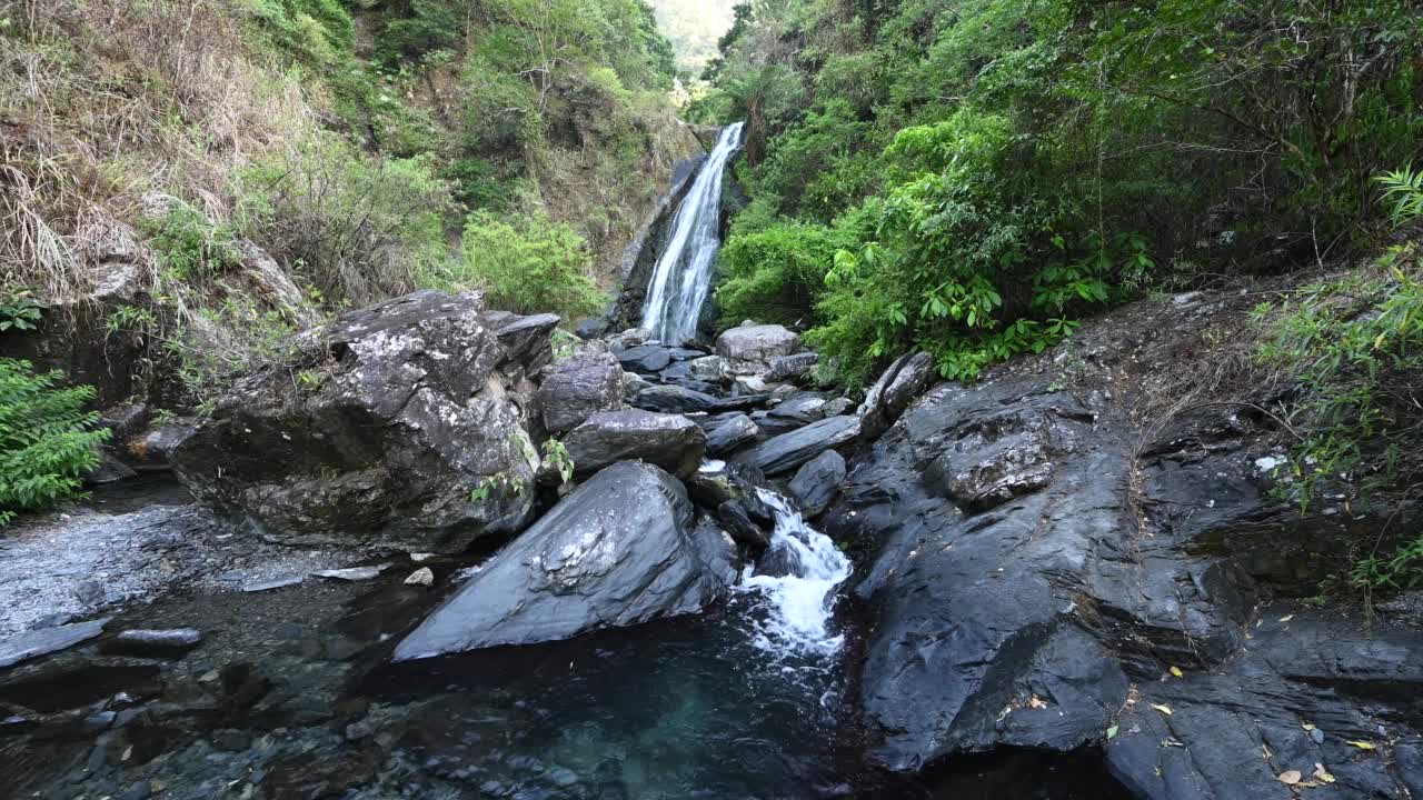 新辽瀑布隐藏在山谷中，阳光照耀在山的后面，绿色的植物和大岩石环绕着瀑布，在台湾宜兰。视频素材