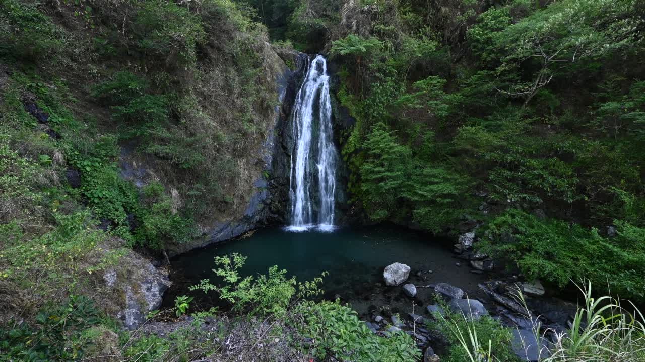 新辽瀑布隐藏在山谷中，阳光照耀在山的后面，绿色的植物和大岩石环绕着瀑布，在台湾宜兰。视频素材