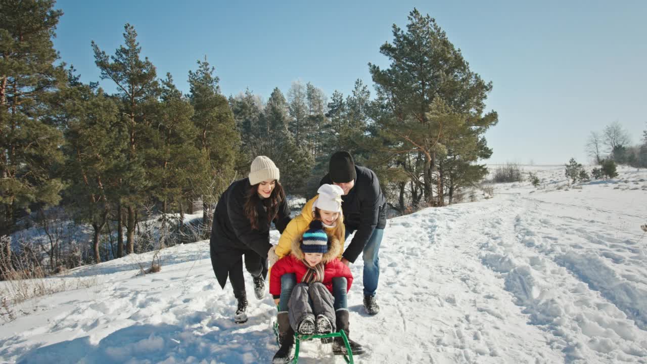 父母帮助孩子从被雪覆盖的山上滑下来视频素材