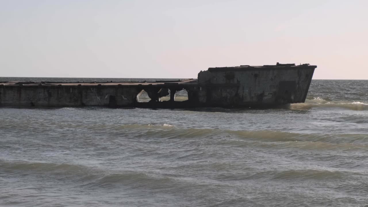 靠近海岸的一艘废弃的混凝土驳船，海浪穿过货船的洞涌向海岸视频素材