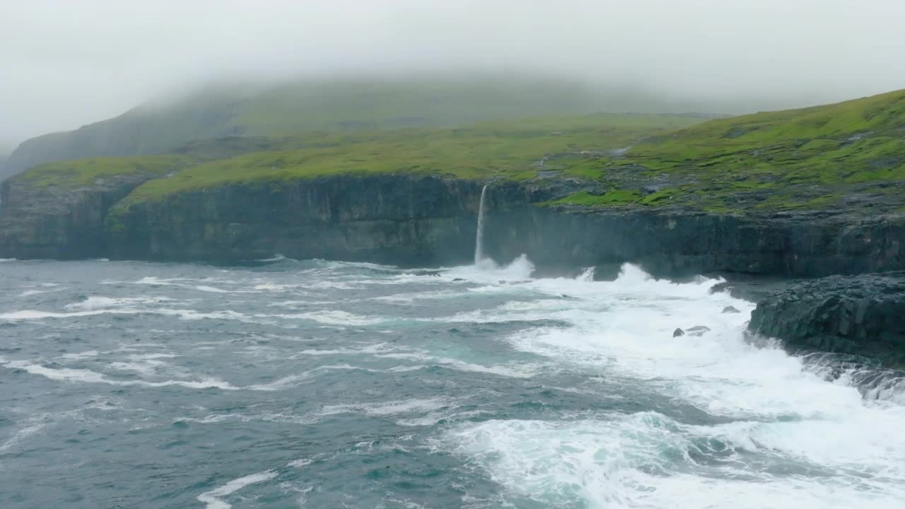 空中慢镜头拍摄悬崖上瀑布的美景，无人机向前飞越海-丹麦法罗群岛视频素材