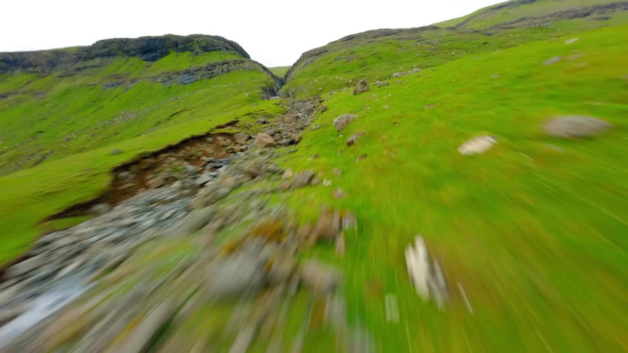 空中拍摄的自然绿色山脉对着天空，无人机在溪流和岩层中飞行-法罗群岛，丹麦视频素材