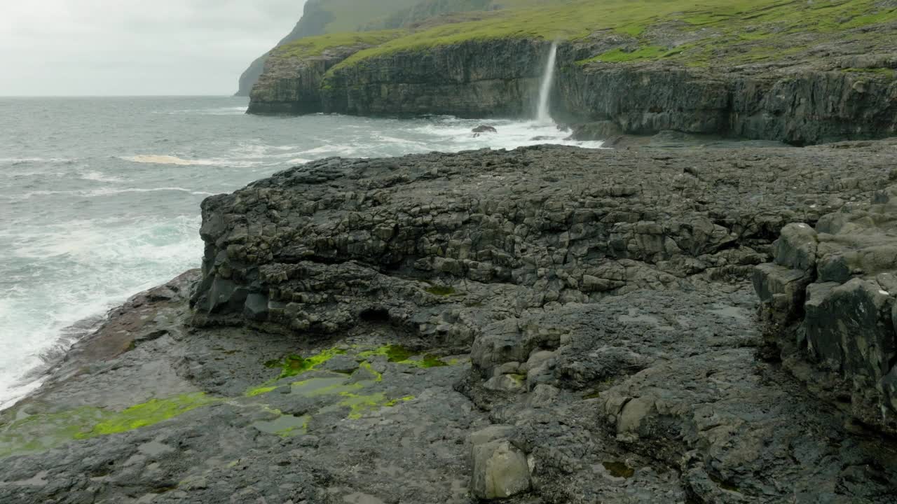 航拍的鸟飞过瀑布上的岛屿，无人机向前飞过波浪的海洋-法罗群岛，丹麦视频素材