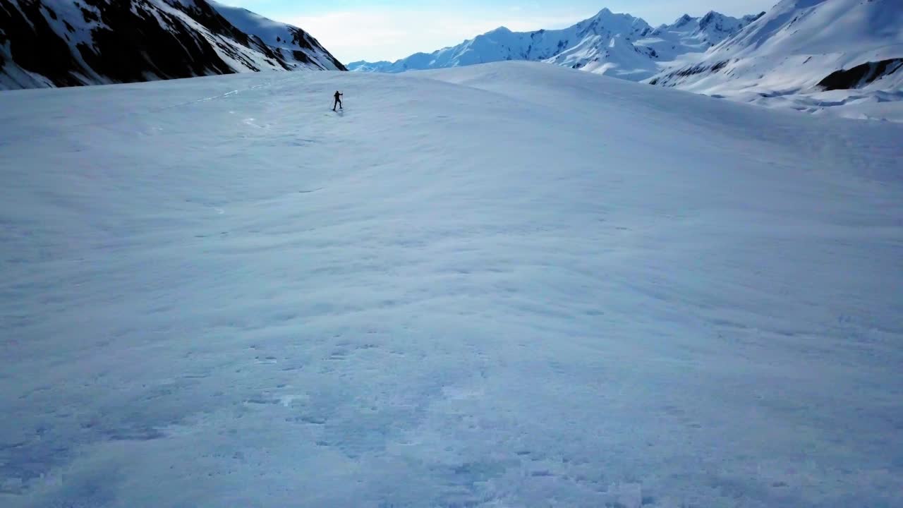 在Canwell冰川的积雪覆盖的土地上，男子用滑雪杖滑雪的航拍镜头视频素材