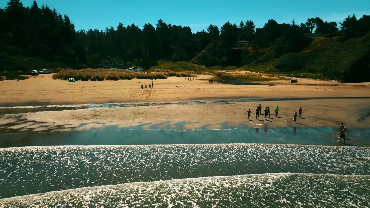 航拍的孩子们在海滩上跑向海浪的大海，无人机在阳光明媚的日子向后飞行-苏斯瓦夫国家森林，俄勒冈州视频素材