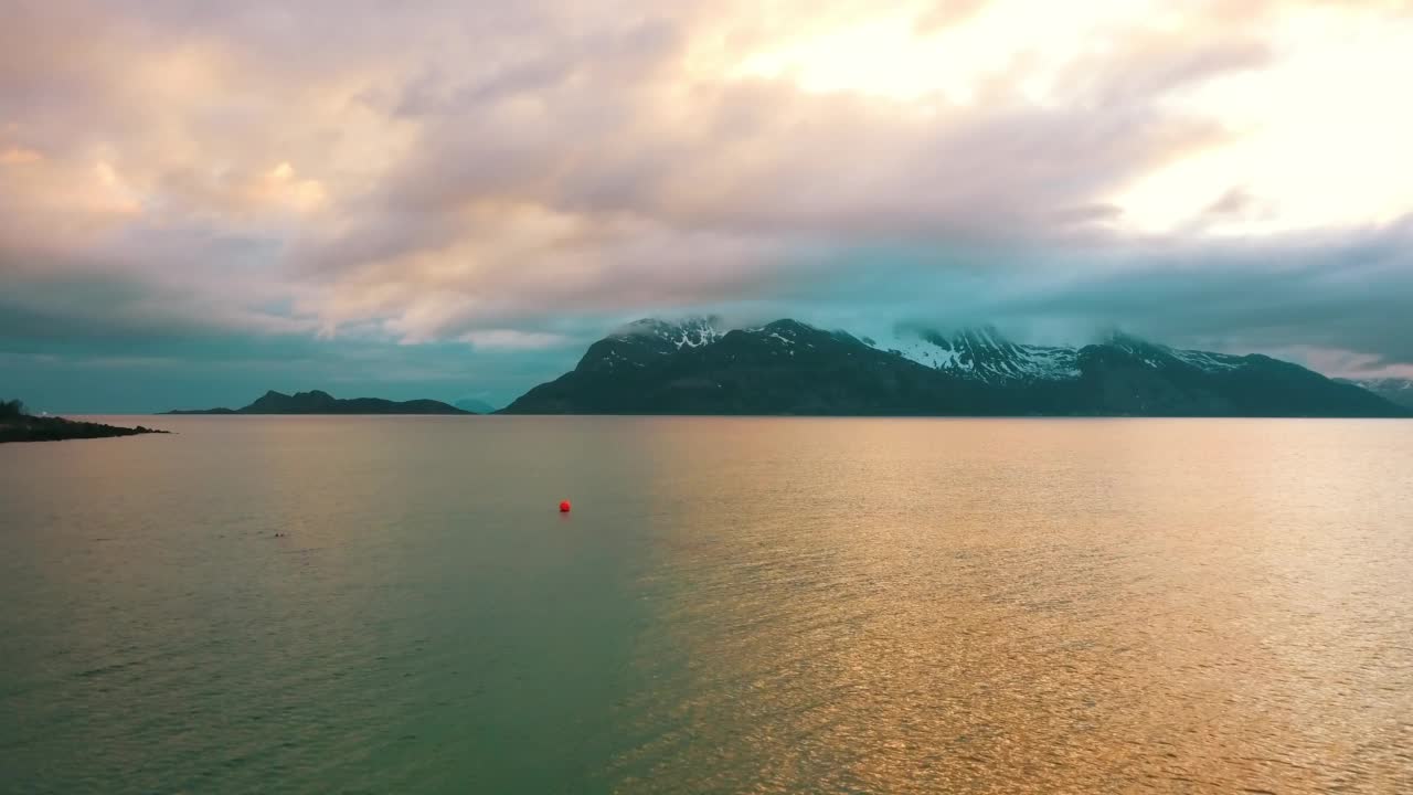 鸟瞰雪山美景，无人机在日落时向后飞过波光粼粼的海面——挪威特罗姆瑟视频素材