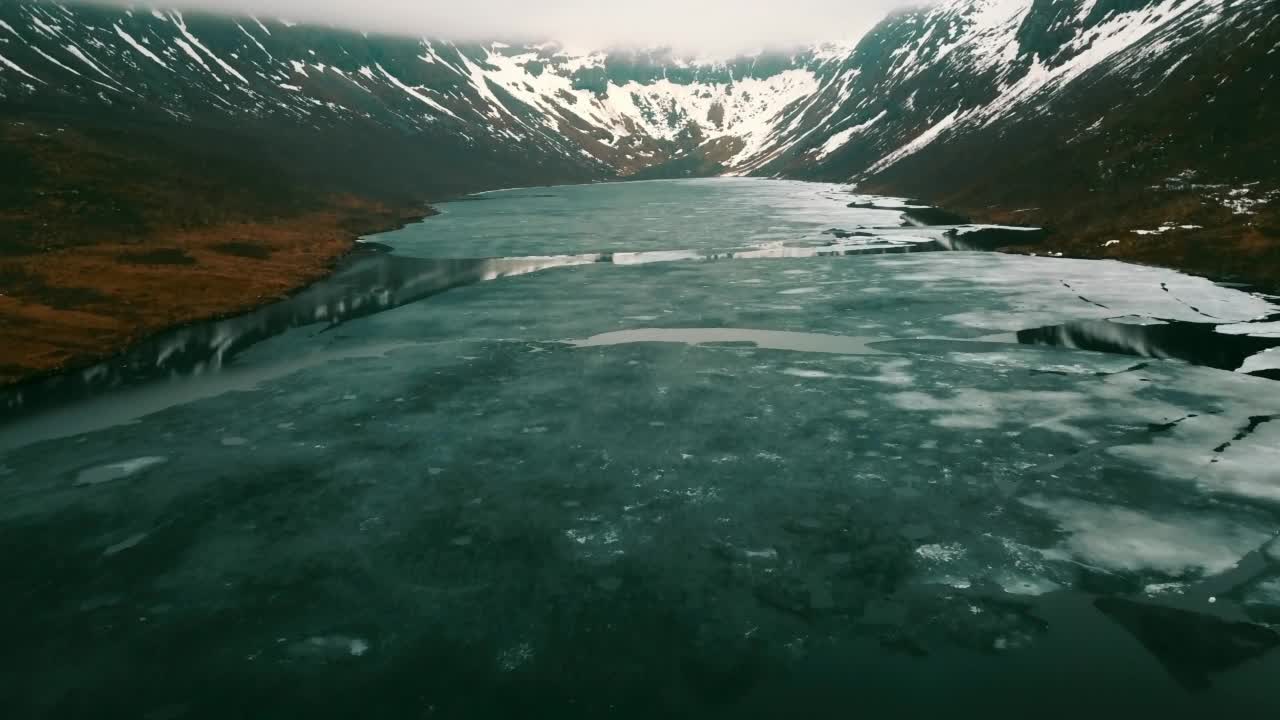 航拍宁静的雪山，无人机向后飞过结冰的湖面-挪威特罗姆瑟视频素材